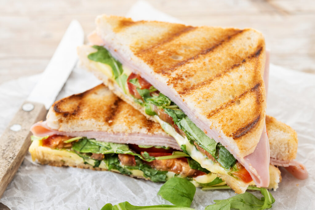 Panini sandwich with ham, cheese, tomato and arugula on wooden t